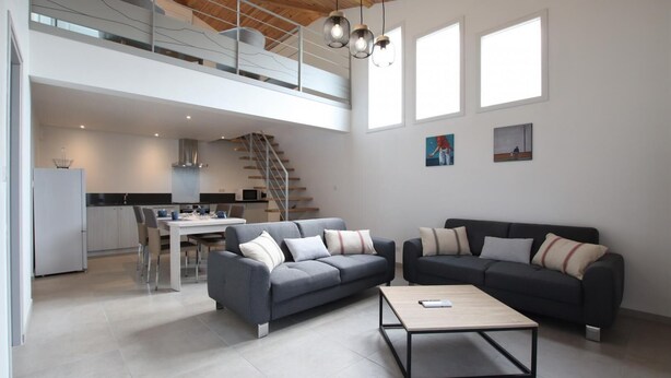 A spacious living area with a grey sofa, a coffee table, and a staircase leading to an upper level. - JOANESENEA BI - SOURAIDE (SOURAIDE)