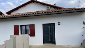 A white building with a tiled roof, a black door, and two windows with red shutters. - JOANESENEA BI - SOURAIDE (SOURAIDE)