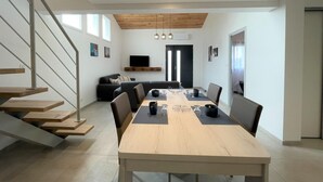 A modern living room with a dining area, wooden staircase, and a flat-screen TV mounted on the wall. - JOANESENEA BI - SOURAIDE (SOURAIDE)