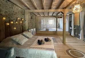 A cozy bedroom with a stone wall, wooden beams, a large bed, and a view of the outdoors. - ELISSABIDE - ESPES-UNDUREIN (ESPES-UNDUREIN)