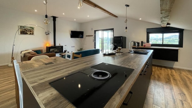 A modern kitchen with a large island, built-in appliances, and a dining area with a sofa and table. - MENDIBURIA - IHOLDY - Gîte (IHOLDY)