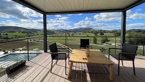 A covered outdoor seating area with a wooden table and chairs, overlooking a scenic landscape with fields and mountains. - MENDIBURIA - IHOLDY - Gîte (IHOLDY)