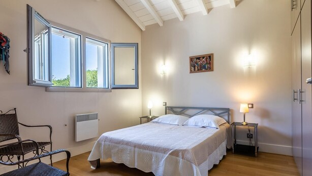 Een slaapkamer met een bed, twee bedlampen, een raam, een radiator, een stoel en een schilderij aan de muur.