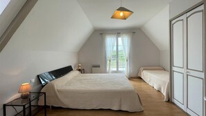 Ein Schlafzimmer mit einem großen Bett, einem kleineren Bett, einem Nachttisch mit Lampe und einer Deckenleuchte.
