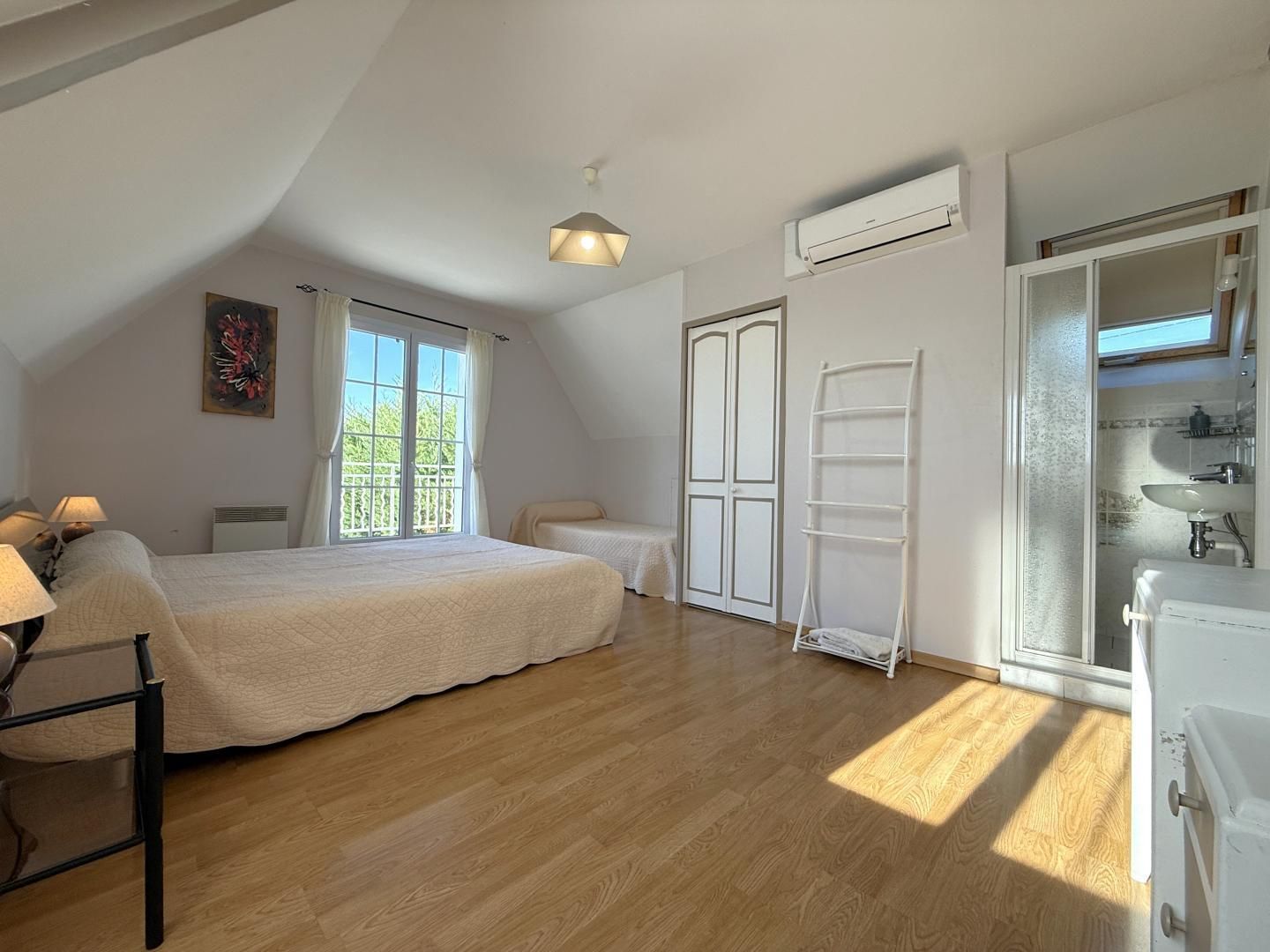 A bedroom with a large bed, a desk, a chair, a ladder, and a bathroom with a sink and mirror.
