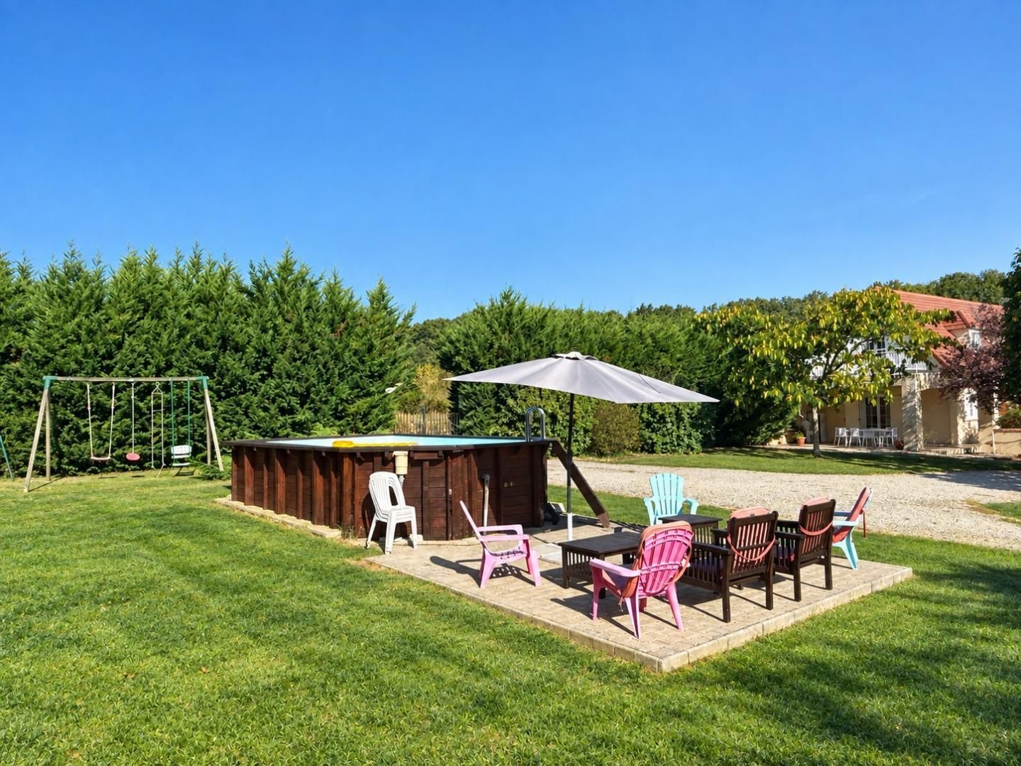 A backyard with a wooden playhouse, outdoor seating, and a swing set.