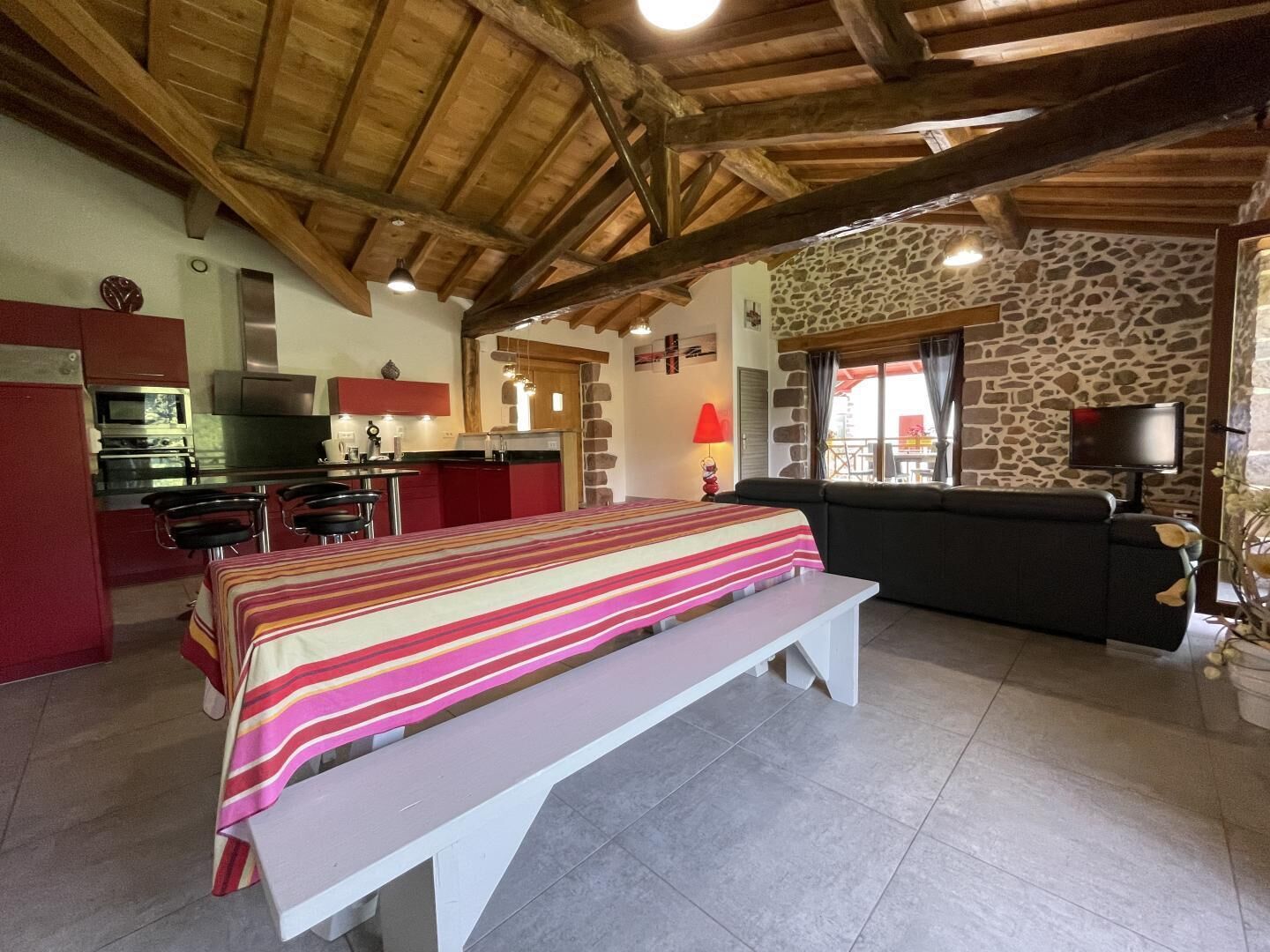 A cozy room with a bed, a bench, a sofa, a kitchen, and a stone wall.