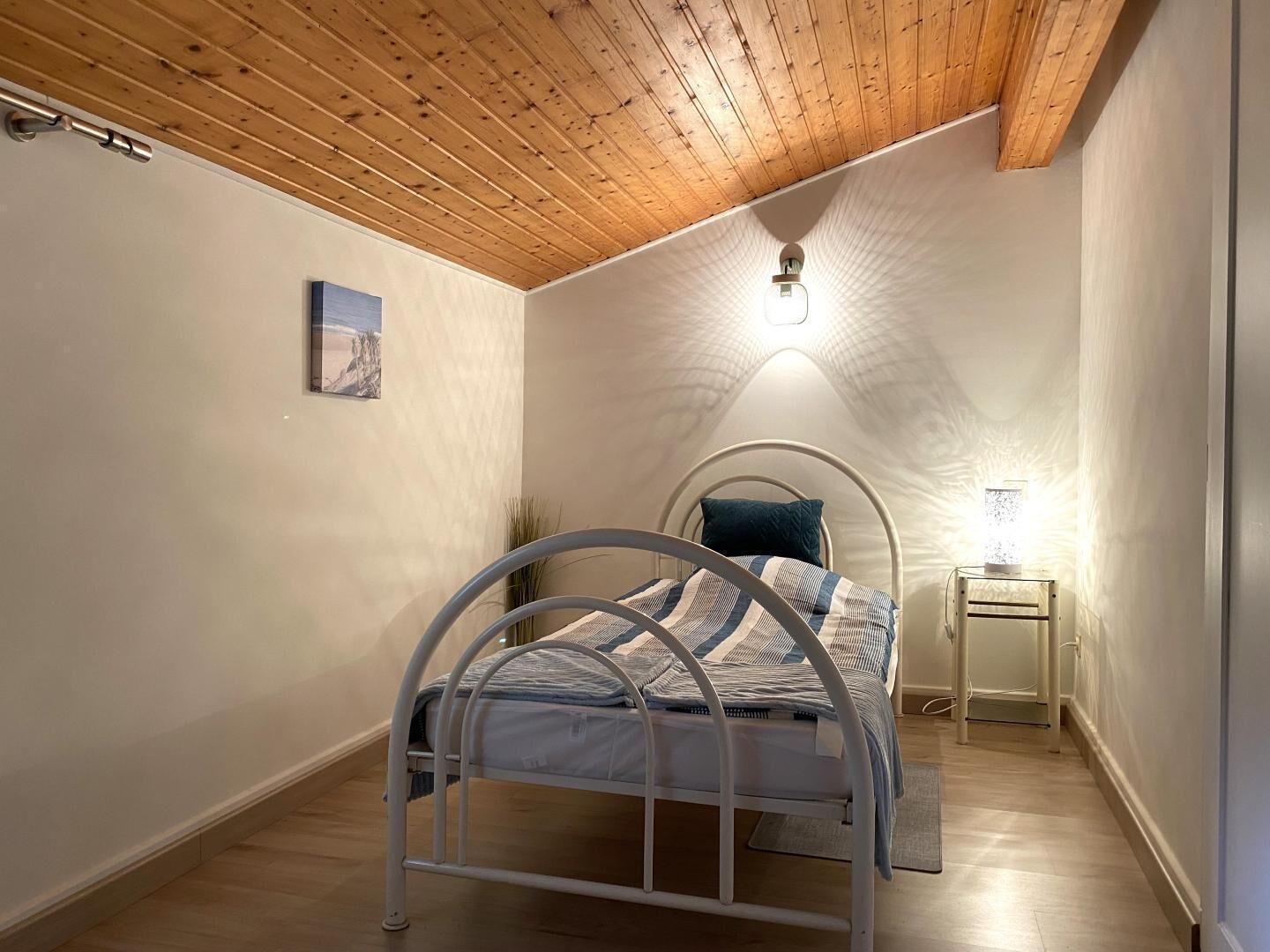 A bedroom with a metal bed frame, a bedside table with a lamp, and a painting on the wall.