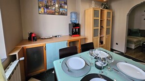 A dining area with a table set for four, a water dispenser, a coffee machine, and a cabinet with shelves.