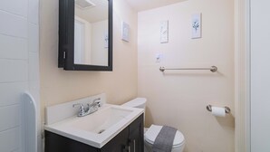 Et badeværelse med hvid vask, spejl, toilet og håndklædetørrestativ.