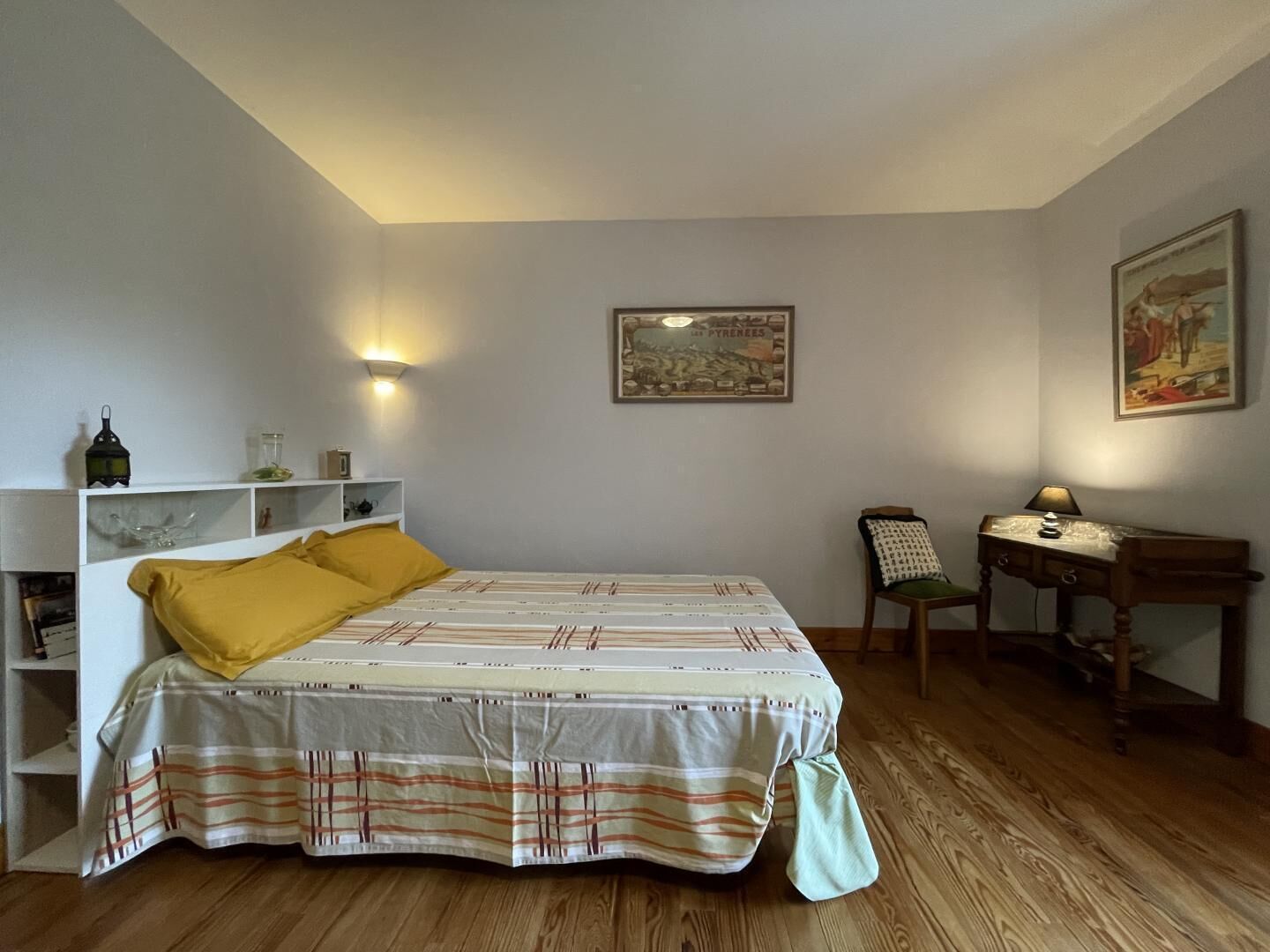 A bedroom with a bed, a desk, a chair, and a shelf with decorative items.