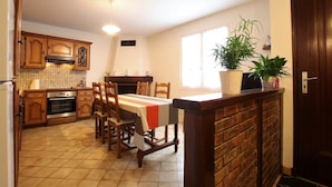 A kitchen with wooden cabinets, a dining table, and chairs. There is a brick wall and a door on the right. - IRIBURU-BERRIA - SARE (SARE)