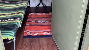 Een kleine, rustieke kamer met een houten wand, een raam, een bed, een tafel en een deur.