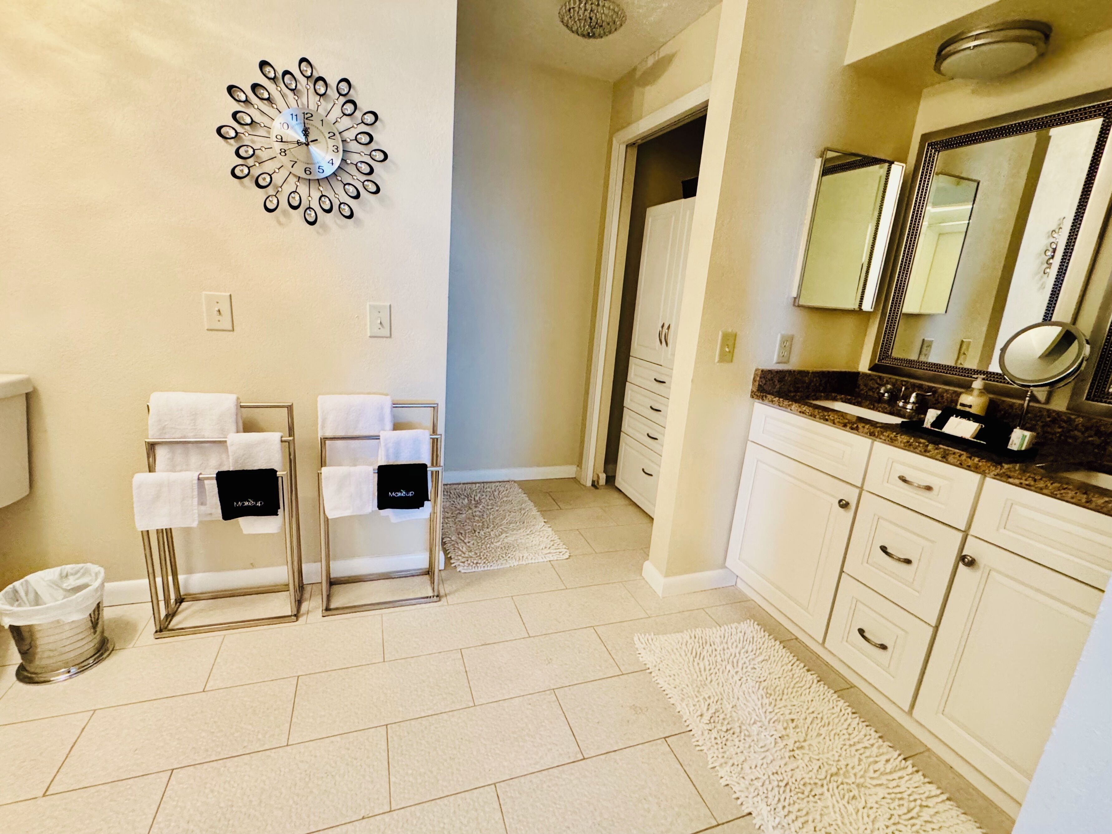 Une salle de bain comprenant un meuble-lavabo, un évier, un miroir, un porte-serviettes et une horloge murale décorative.