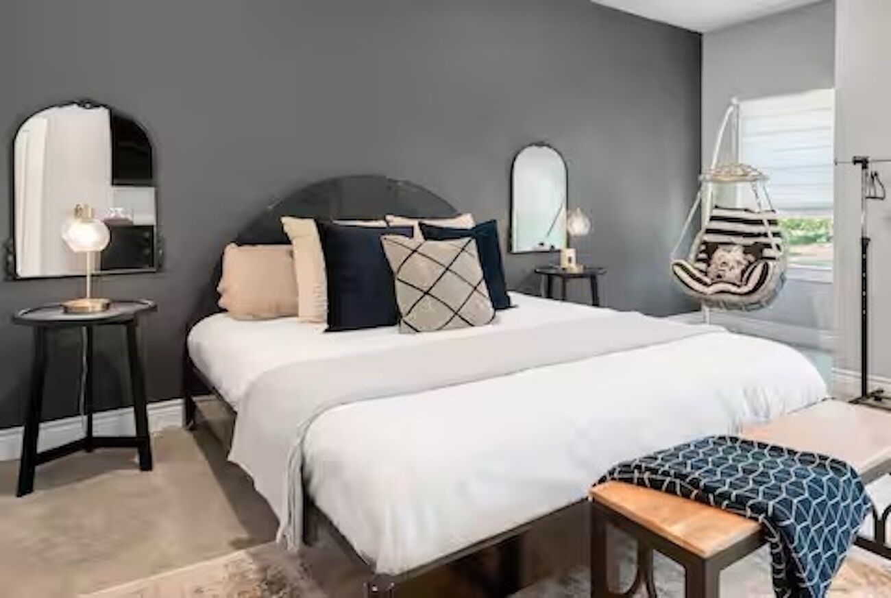 Une chambre à coucher avec un lit, des tables de chevet, un fauteuil suspendu et une grande fenêtre.