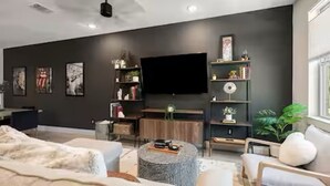 A modern living room with a flat-screen TV, a bookshelf, a coffee table, and a sofa. - The Hard Rock Condo! (Bryan)