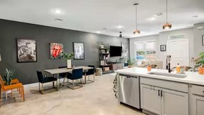 A modern kitchen with a central island, a dining area with a table and chairs, and a living space with a sofa and a TV. - The Hard Rock Condo! (Bryan)