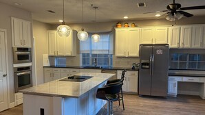 A modern kitchen with white cabinets, stainless steel appliances, a large island with bar stools, pendant lighting, and a ceiling fan. - Soothing 4-bedroom house with AC in charming Plano (Plano)