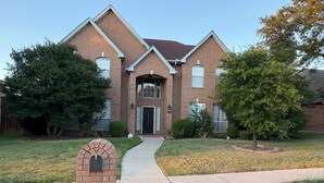 A two-story brick house with a central entrance, a front yard with a pathway, and a mailbox. - Soothing 4-bedroom house with AC in charming Plano (Plano)