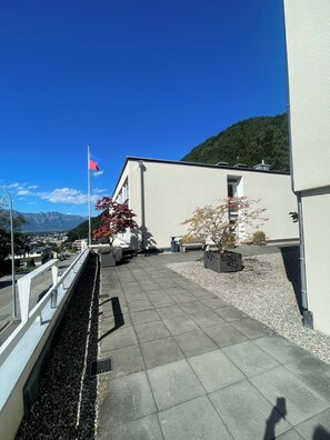 A rooftop terrace with a flag, potted plants, and a view of a town and mountains. - Comfortable vacation apartment in Triesen (Triesen)