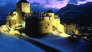 Un château médiéval doté d’une tour imposante, entouré d’un paysage enneigé et illuminé par des éclairages artificiels.