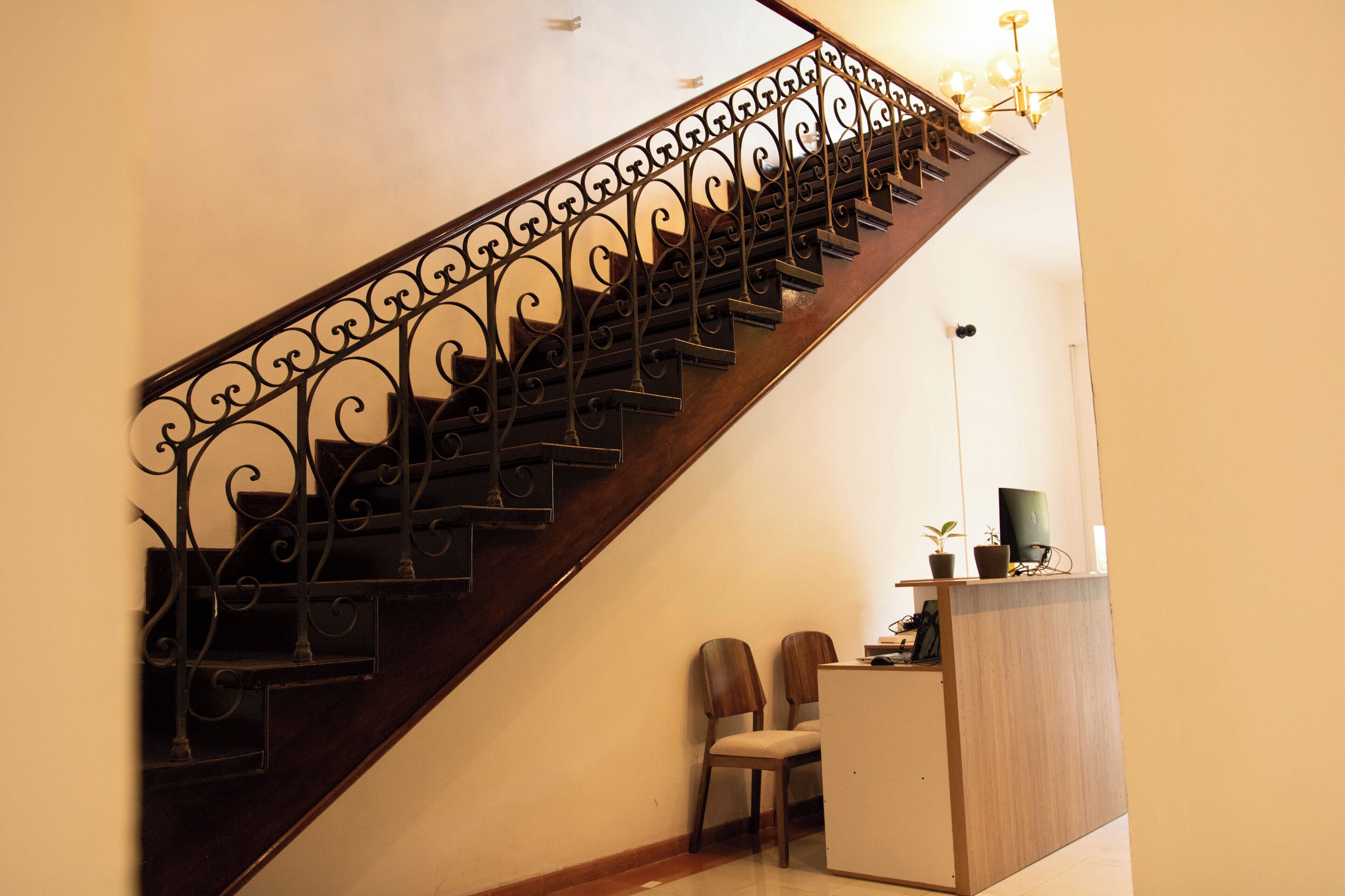 Una escalera de madera con barandillas de metal decorativas, un escritorio pequeño con un ordenador y dos sillas.