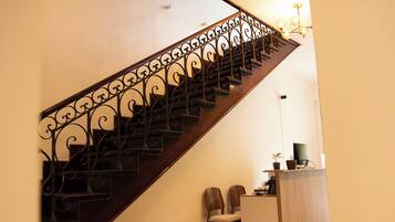 Una escalera de madera con barandillas de metal decorativas, un escritorio pequeño con un ordenador y dos sillas.