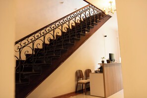 Eine hölzerne Treppe mit aufwendiger Metallreling, ein kleiner Schreibtisch mit einem Computer und zwei Stühle.