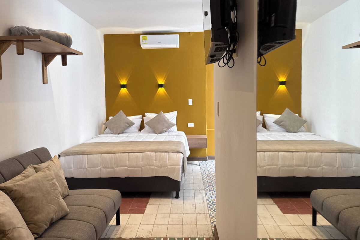 A hotel room with two beds, a sofa, an air conditioning unit, and a television.