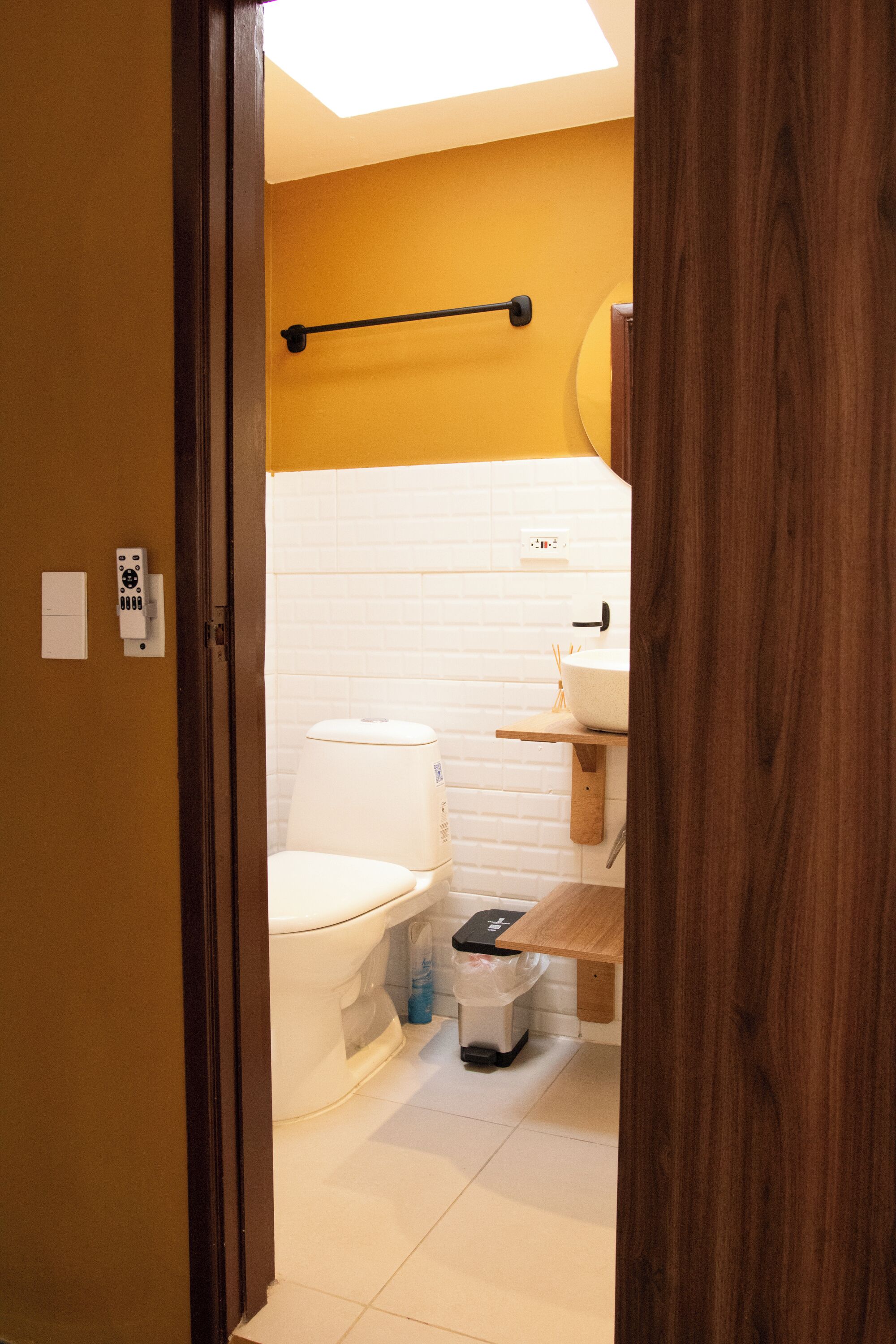 A bathroom with a toilet, a white sink, and a wooden shelf.