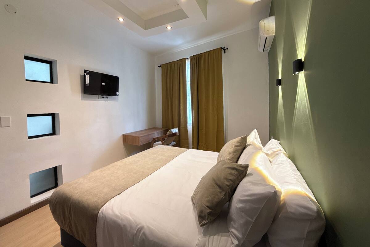 A hotel room with a bed, a desk, a television, and a window with curtains.