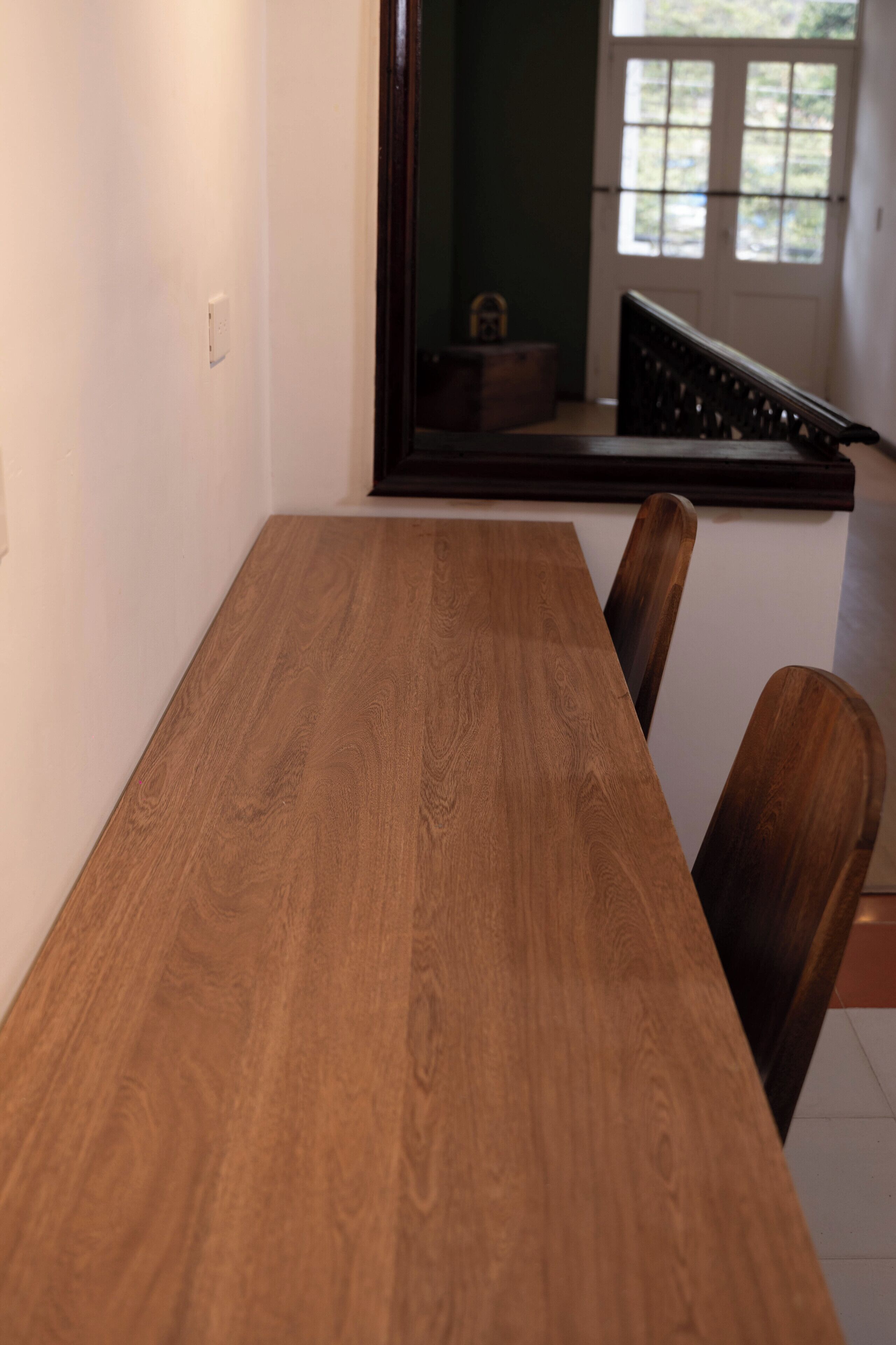 Ein Holzespeisetisch mit Stühlen, eine weiße Wand und Blick auf eine Treppe und ein Fenster.