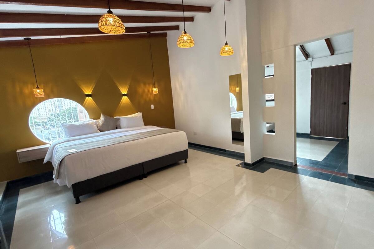 A modern bedroom with a large bed, a circular window, and pendant lighting.