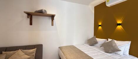 A bedroom with a bed, a sofa, a wooden shelf, and wall-mounted lights.