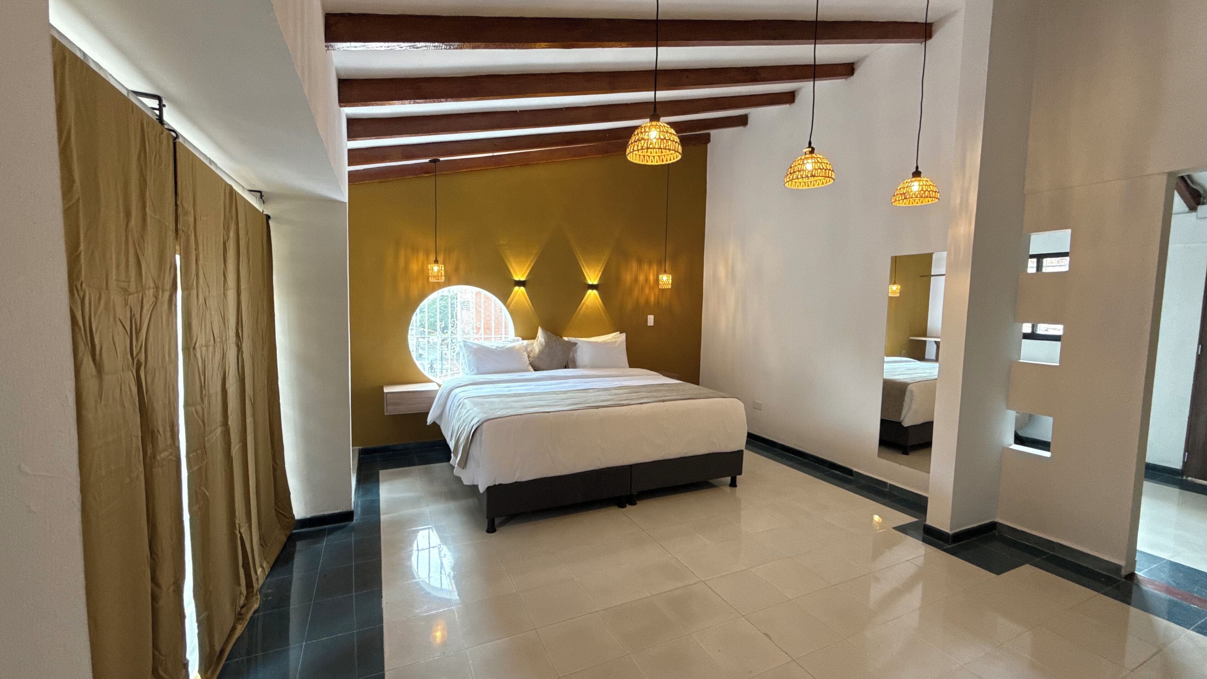A modern hotel room with a large bed, a bedside table, a mirror, and a window with curtains.