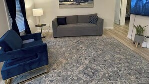 A modern living room with a grey sofa, blue armchair, patterned rug, ceiling fan, and a TV on the wall. - Charming 2-bedroom condo in lovely Springfield with AC (Springfield)