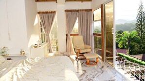 A bedroom with a bed, a chair, and a view of greenery through large windows. - Paradise  villa (Pedro Brand)