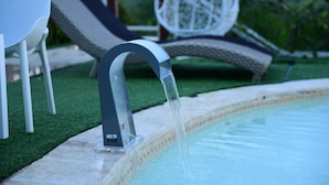 A modern outdoor pool with a clear water feature, surrounded by a well-maintained lawn and outdoor furniture. - Paradise  villa (Pedro Brand)