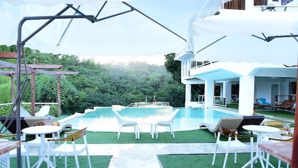 A modern outdoor pool area with white furniture and a view of a lush green landscape. - Paradise  villa (Pedro Brand)