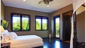 Una camera da letto con un letto, una ventola a soffitto, due finestre e una porta che dà su un balcone.