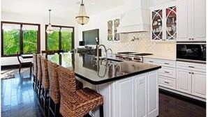 Una cucina moderna con mobili bianchi, una grande isola con sgabelli da bar e vista sul verde attraverso ampie finestre.