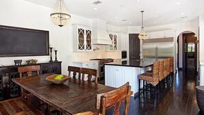 Un'ampia cucina con una grande isola, un tavolo da pranzo in legno scuro e moderna illuminazione a sospensione.