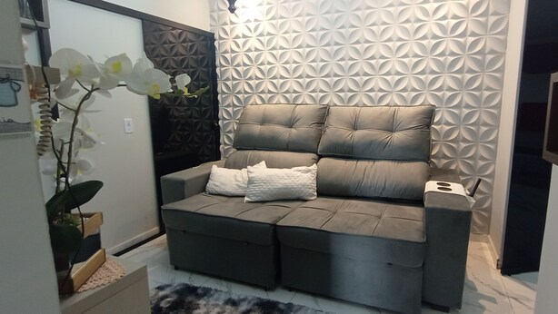 A modern living room with a grey sectional sofa, a decorative wall with geometric patterns, and a white orchid plant. - Ksl bird refuge (Araquari)