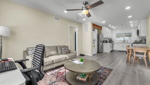 Uma sala de estar moderna com sofá, mesa de centro redonda, escrivaninha com computador e área de jantar com cadeiras e mesa.