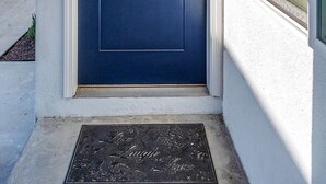 Uma porta azul com uma pequena janela acima, um tapete de entrada com as palavras “Laugh Love” e uma parede branca com uma janela à direita.