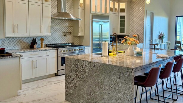 Moderni keittiö, jossa on suuri keittiösaareke, ruostumattomasta teräksestä valmistetut kodinkoneet ja riippuvalaisimet.