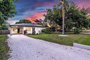 A single-story house with a gravel driveway, surrounded by a well-maintained lawn and trees. - Gulf Gate Retreat | Private Back Yard + Grill (Sarasota)