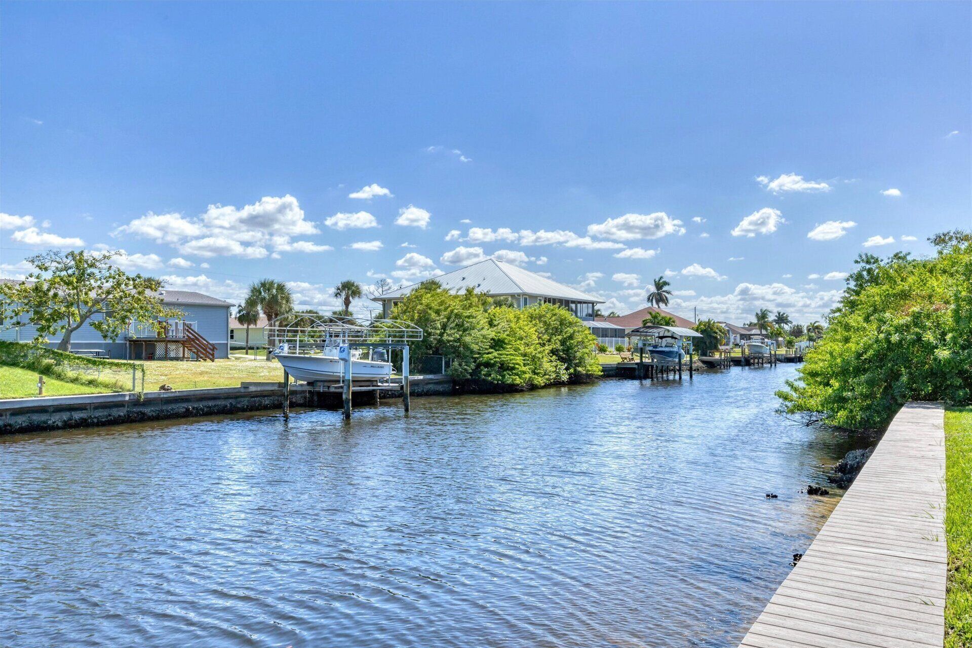 A canal with boats docked on the right, surrounded by residential houses and greenery.