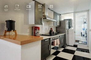 Une cuisine moderne avec un sol à carreaux noirs et blancs, des appareils en acier inoxydable et une machine à café posée sur le plan de travail.