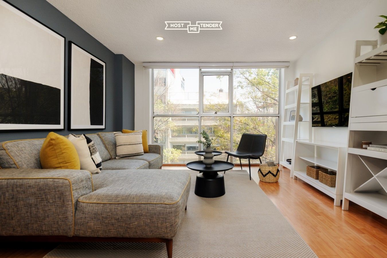 A modern living room with a grey sofa, a black coffee table, and a bookshelf.